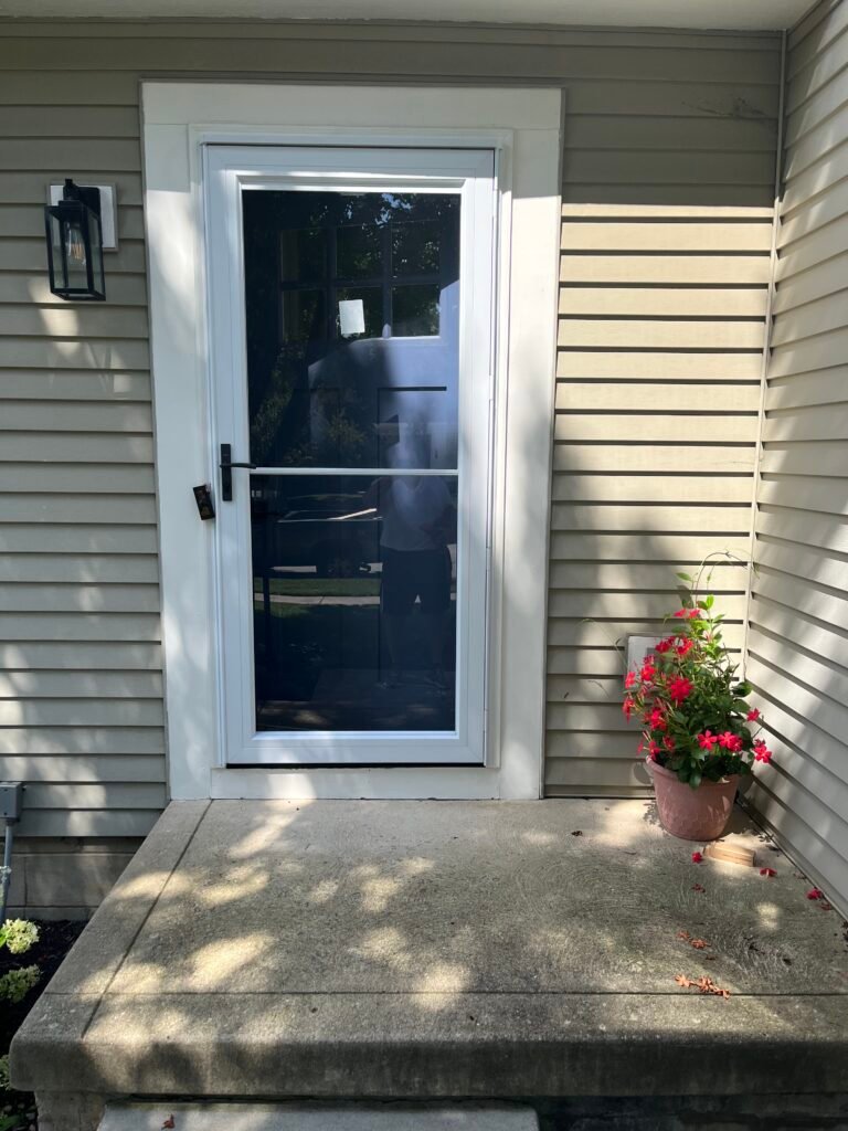 White-framed storm door at a gray-sided home entrance